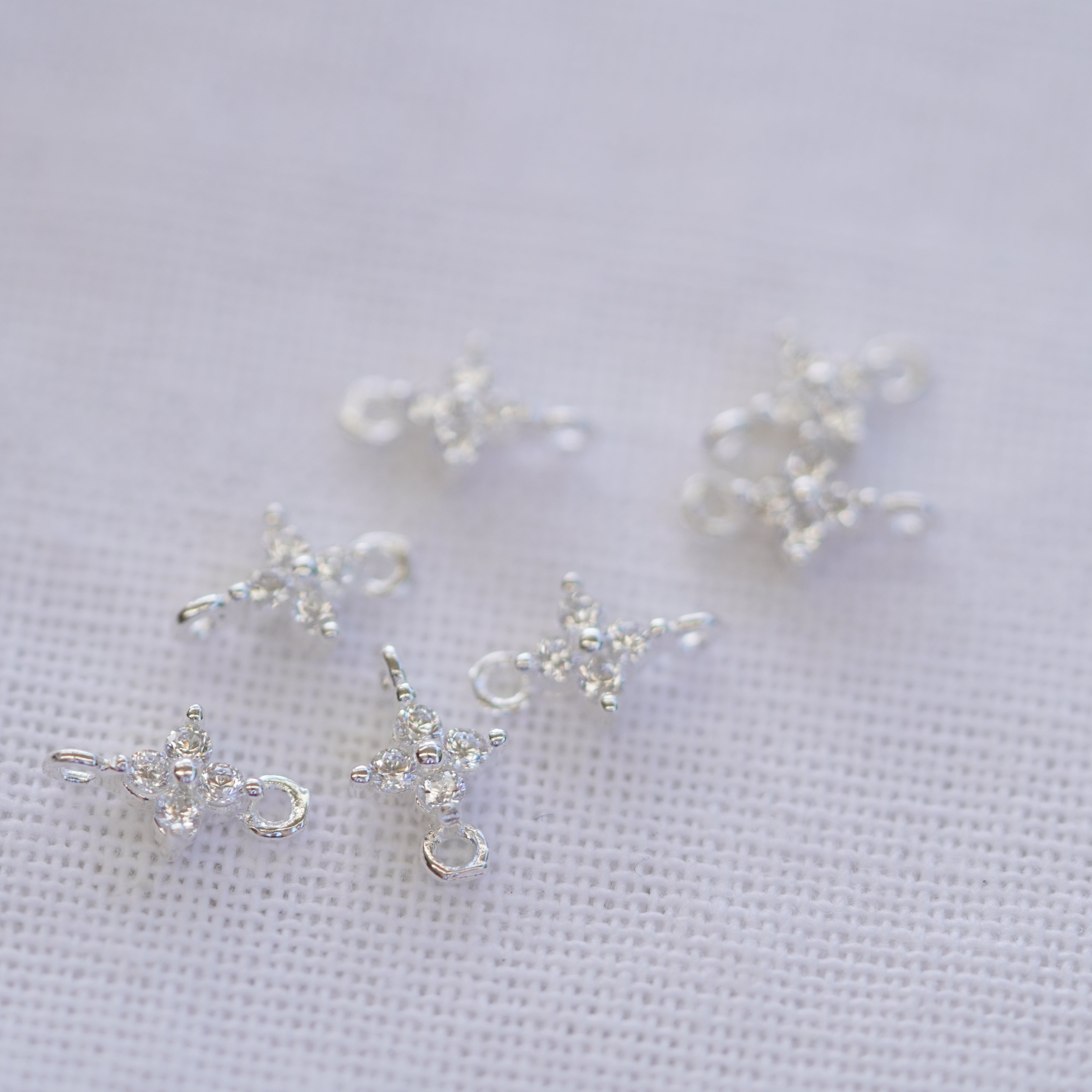 Small sterling silver charms shaped like flowers with zircon stones on a white background